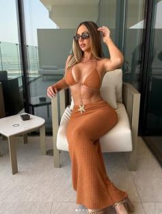 Woman in a rust-colored bikini and matching maxi skirt sitting on a chair on a balcony.