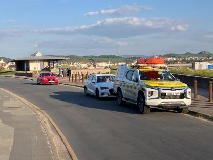 Coastguard vehicle and cars near a beach.