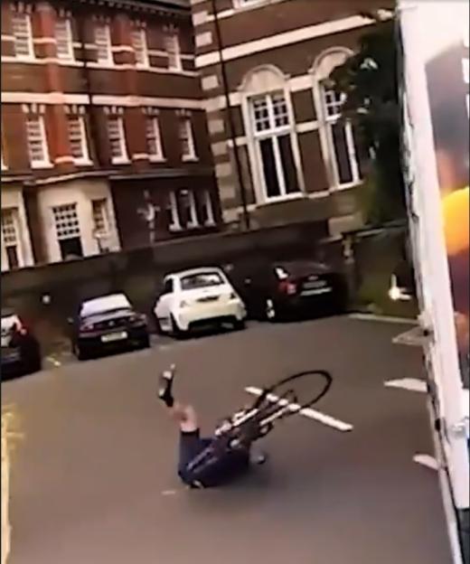 Cyclist fallen on the road next to a white van and parked cars.