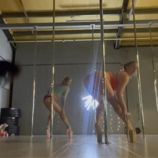Two women pole dancing in a studio.
