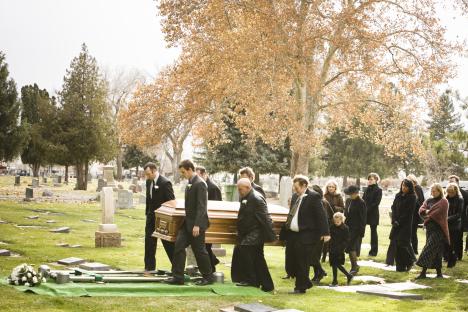 Pallbearers carrying a casket at a funeral in a cemetery.