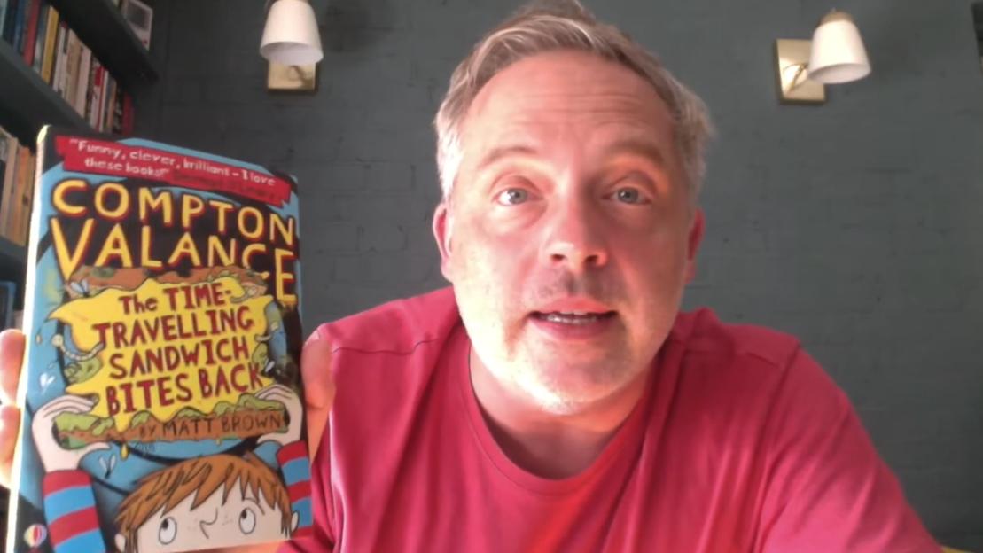 TV presenter and radio broadcaster Matt Brown holding up his book, "Compton Valance: The Time-Travelling Sandwich Bites Back."