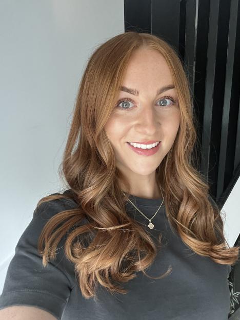 A woman with long, shiny, wavy red hair smiles at the camera.