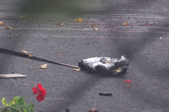 Device with wires taped to it on asphalt, with smoke and red debris nearby.