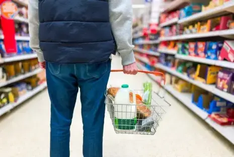 Person in a supermarket pushing a shopping basket with groceries.