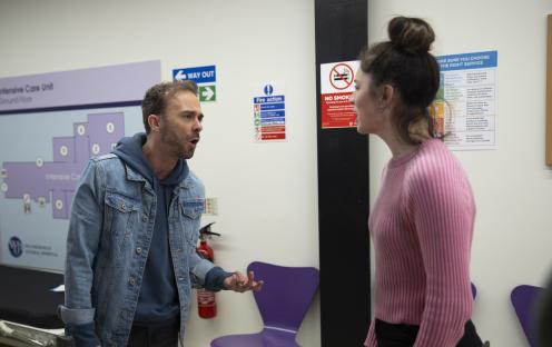 A man and woman arguing in a hospital hallway.