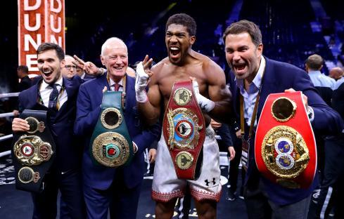 Anthony Joshua posing with boxing championship belts and associates.