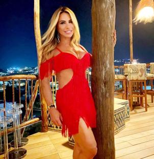 Woman in red fringed dress leaning against a wooden post.
