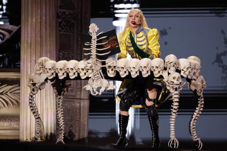 Lady Gaga performing at Copacabana Beach, seated at a piano made of skulls and skeletons.