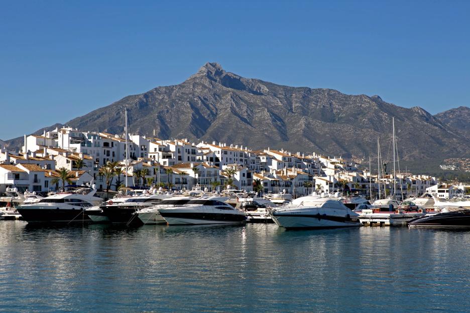 Puerto Banus with luxury yachts, white buildings, and a mountain in the background.