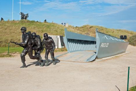 WWII memorial at Utah Beach Landing Museum, Normandy, featuring statues of soldiers and a Higgins boat.