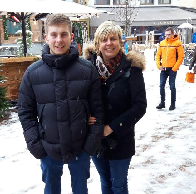 A young man and woman smiling at the camera in a snowy outdoor setting.