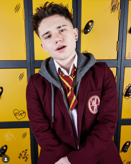 Young person in a school uniform, with an open mouth, standing in front of yellow lockers.