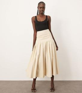 Woman wearing a black tank top and a beige pleated midi skirt.