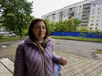 Woman in purple jacket standing outside apartment building.