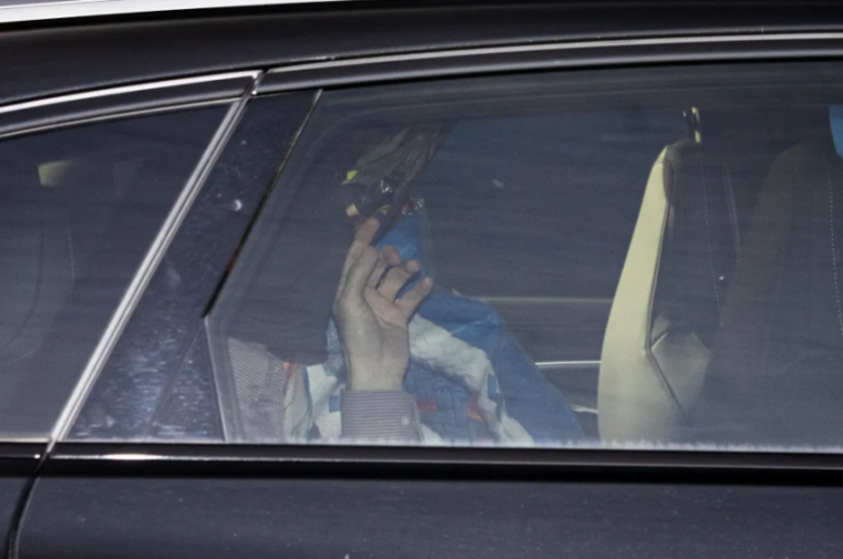 Person holding a blue and white flag in the back seat of a car.