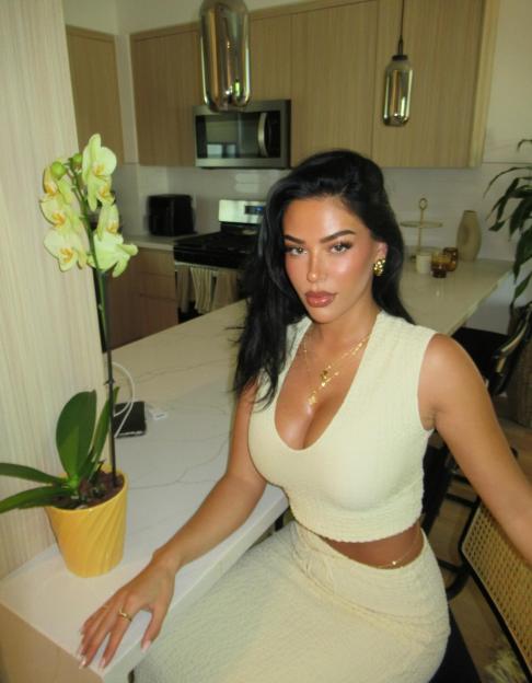 Woman in a cream-colored outfit sitting at a kitchen counter.