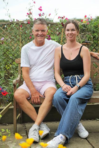 A man and woman sit on a bench in a garden.