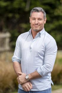 Dean Gaffney, smiling and wearing a light blue shirt.