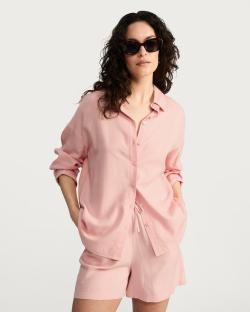 Woman wearing a pink linen shirt and shorts.