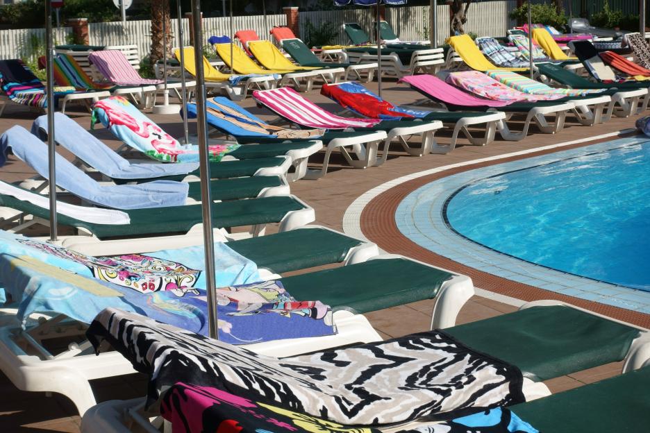 Empty lounge chairs with colorful towels surround a swimming pool.