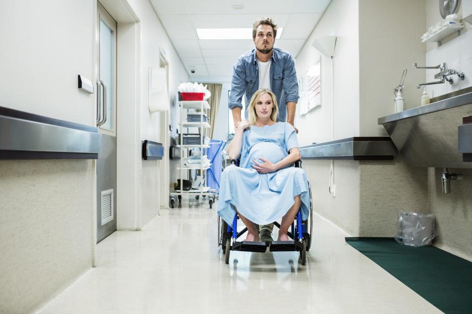 Pregnant woman in a wheelchair being pushed by a man down a hospital corridor.