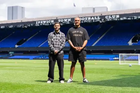 Two men standing on a soccer field in front of a stadium.