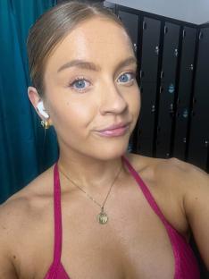 Woman in pink sports bra, wearing earrings and a necklace, in front of lockers.