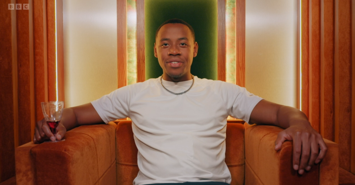 A man sits in an orange chair, holding a small glass.
