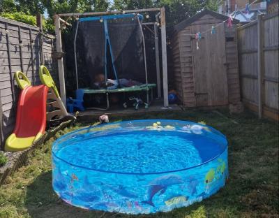 A paddling pool in a backyard with a trampoline and slide.