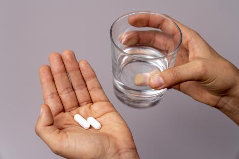 Hand holding two pills and a glass of water.