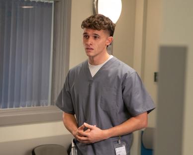 Jacob Gallagher in a gray scrubs in an Emmerdale scene.