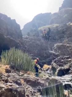 Rescuers airlifting a body from a rocky area.