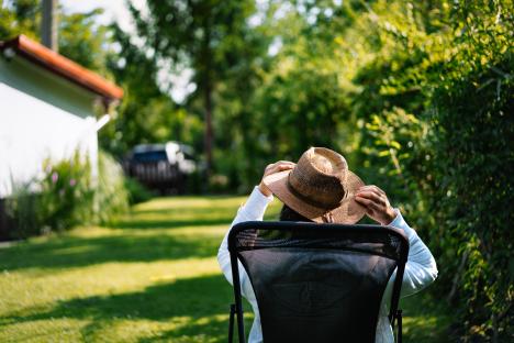 Person sitting in a chair outdoors, adjusting their straw hat.