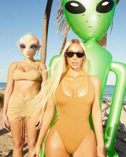 Kim Kardashian in a tan one-piece swimsuit with two models wearing alien masks and a large inflatable alien.