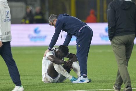A dejected soccer player sits on the field while his coach comforts him.
