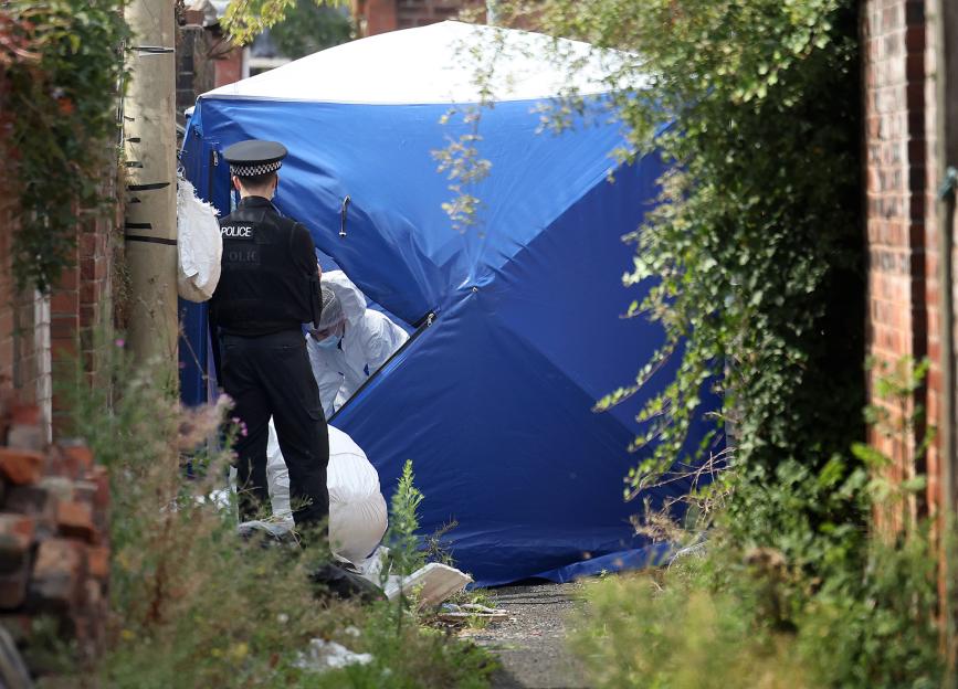 Police officer standing by a forensic tent in an alleyway.