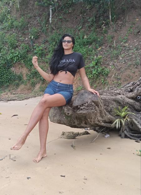 Woman sitting on a log on a sandy beach.