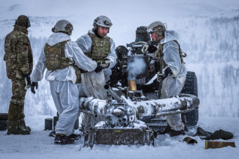 Soldiers in white camouflage operating a howitzer in snowy conditions.