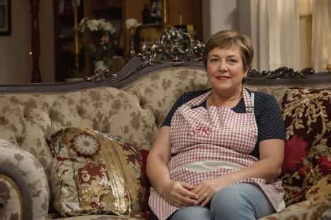 Woman in an apron sitting on an ornate couch.