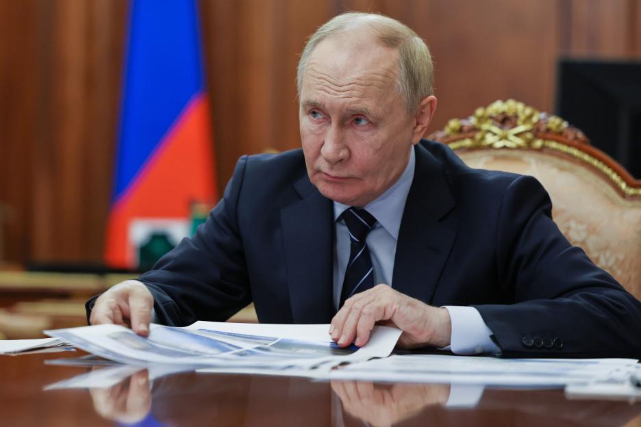Russian President Vladimir Putin in a suit and tie listening intently at a meeting.