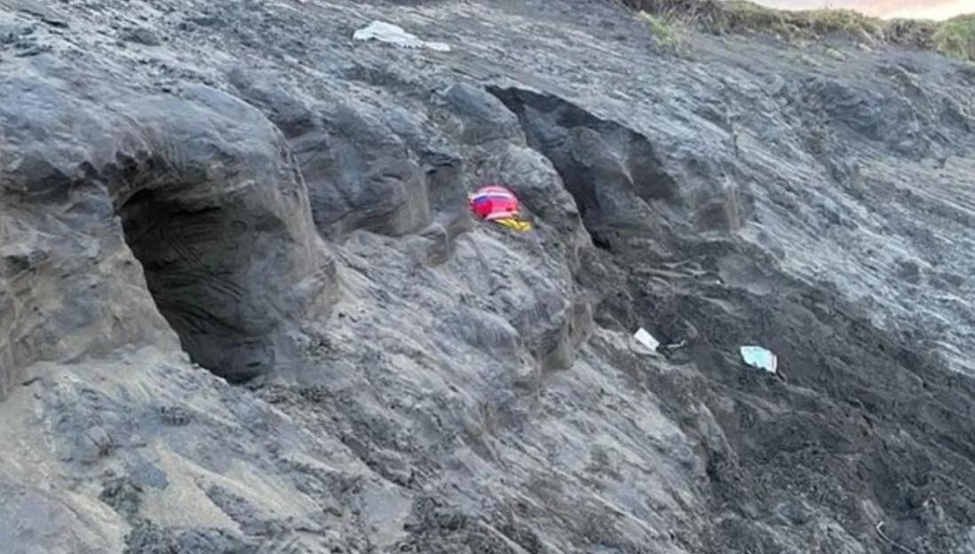 Sand dune collapse at beach, near children's belongings.
