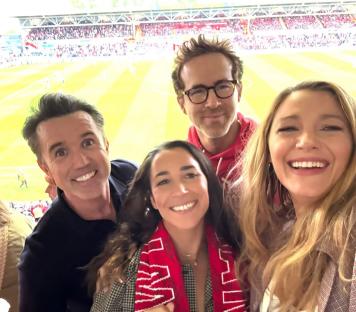 Four people smiling for a selfie at a soccer stadium.