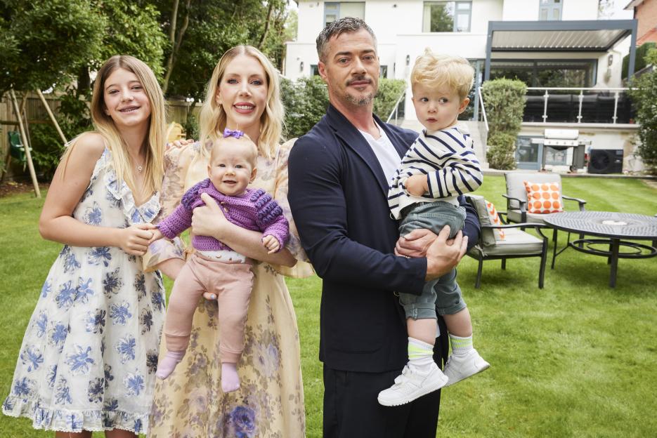 Katherine Ryan and her family, husband Bobby Koostra and children Violet, Fred, and Fenna, stand in a backyard.