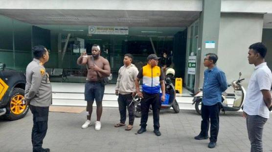 A British tourist, injured and shirtless, speaks with police officers in Bali after a road rage incident.