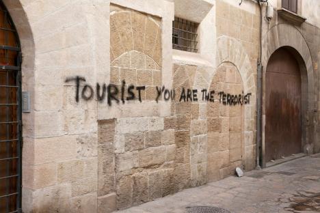 Graffiti on a stone wall reading "Tourist You Are The Terrorist".