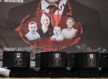 Four caskets containing the bodies of Israeli victims are displayed, with images of the victims and Benjamin Netanyahu depicted on the caskets.