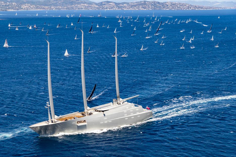 A large sailing yacht called "White Pearl" or "Sailing Yacht A" passes a fleet of sailboats during a race.