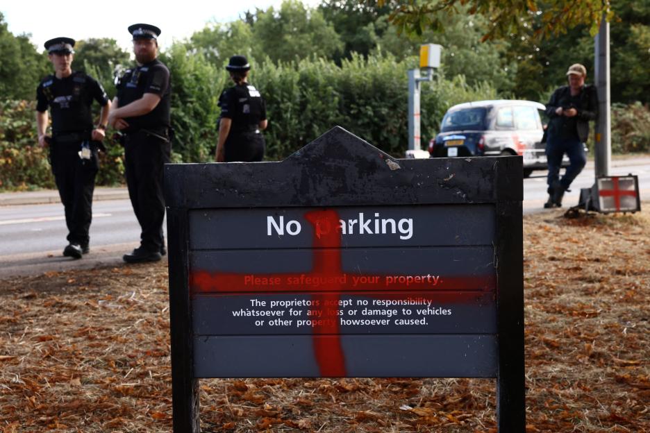 Vandalized "No Parking" sign with St. George's flag in background.