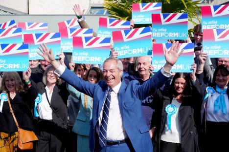 Nigel Farage on the campaign trail, surrounded by supporters holding "I'm voting Reform UK" signs.